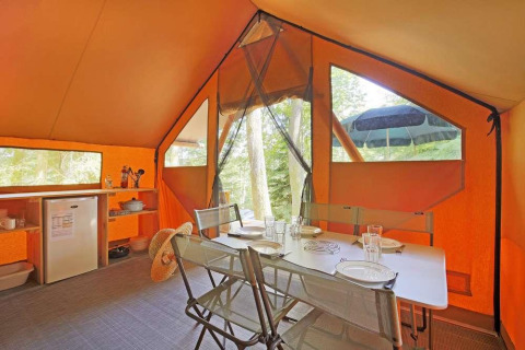 Interior de una tienda safari Canadienne con mesa de comedor y pequeña cocina en Huttopia Wattwiller, Francia