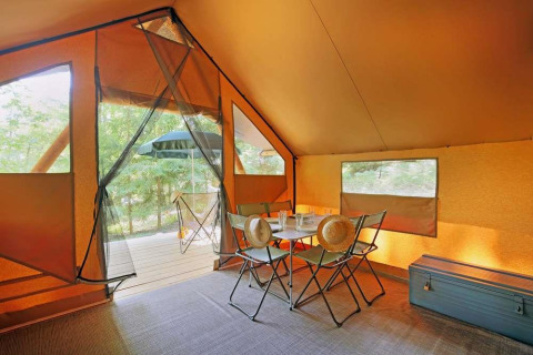Vista interior de una tienda Canadienne en Huttopia Wattwiller, Francia, con mesa y sillas de camping.