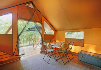 Vista interior de una tienda Canadienne en Huttopia Wattwiller, Francia, con mesa y sillas de camping.