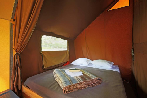Interno di una tenda safari Canadienne a Huttopia Wattwiller, Francia, con letto accogliente e finestra.