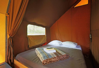 Innenaufnahme eines Canadienne Safari-Zeltes bei Huttopia Wattwiller in Frankreich, mit gemütlichem Bett.