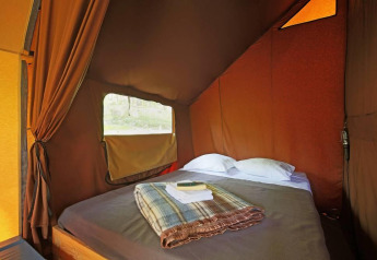 Interior of a Canadienne safari tent at Huttopia Wattwiller, France, showing a cozy bed and window.