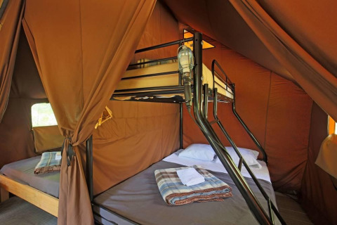 Interior de una tienda safari Canadienne con litera y cama doble en Huttopia Wattwiller, Francia.