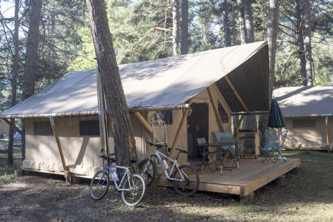 Safari-Zelt Trappeur mit Holzterrasse, zwei Fahrrädern und Campingmöbeln im Wald bei Huttopia Wattwiller.