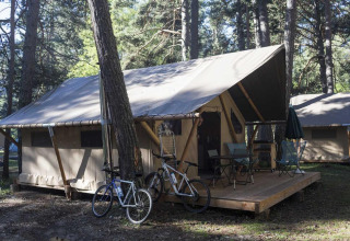 Tienda safari Trappeur con terraza de madera, dos bicicletas y sillas de camping en Huttopia Wattwiller, Francia.
