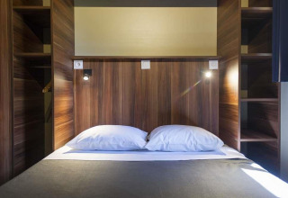 Interior de dormitorio con cama doble, cabecero de madera y estanterías en Chalet Evasion en Huttopia Wattwiller.