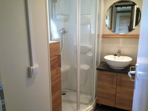 Baño moderno con cabina de ducha, lavabo blanco y espejo redondo en Chalet Evasion en Huttopia Wattwiller.