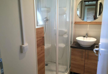 Salle de bains moderne avec douche vitrée, vasque et miroir rond au Chalet Evasion, Huttopia Wattwiller.