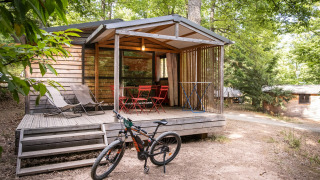 Chalet Evasion træhytte med terrasse, cykel, liggestole og havemøbler i skovklædt omgivelser.