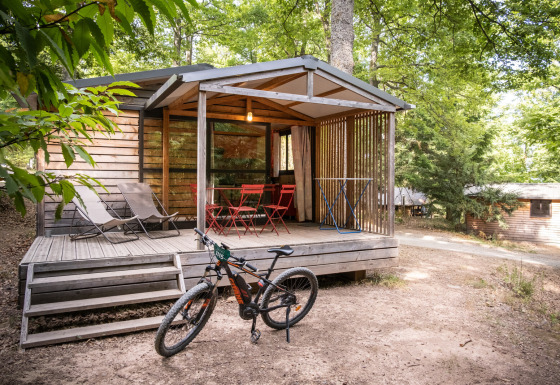Chalet Evasion houten huisje met veranda, fiets, ligstoelen en tuinmeubilair in bosrijke omgeving.