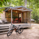 Chalet Evasion træhytte med terrasse, cykel, liggestole og havemøbler i skovklædt omgivelser.