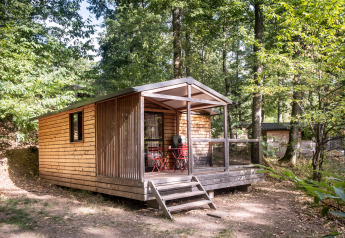 Træhytte Chalet Evasion ved Huttopia Wattwiller, Frankrig, omgivet af grøn skov og sollys.
