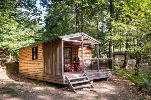 Træhytte Chalet Evasion ved Huttopia Wattwiller, Frankrig, omgivet af grøn skov og sollys.