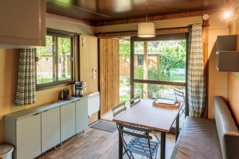 Interior view of Chalet Evasion cabin at Huttopia Wattwiller, France, featuring dining table and garden view.