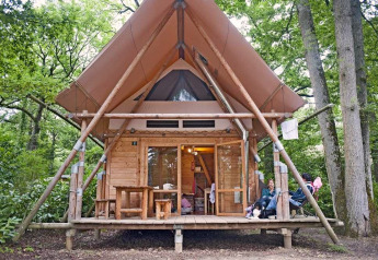 Ein Cahutte Safari-Zelt im Wald mit Holzverkleidung, Überdachung und Menschen, die draußen entspannen.