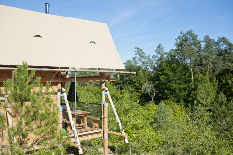 Tienda safari Cahutte en Huttopia Wattwiller, Francia, con terraza de madera y vistas al bosque verde.