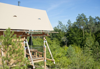 Tienda safari Cahutte en Huttopia Wattwiller, Francia, con terraza de madera y vistas al bosque verde.
