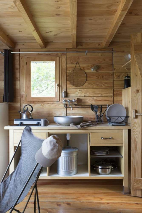 Pequeña cocina de madera con fregadero y utensilios en una tienda safari en Huttopia Wattwiller, Francia.