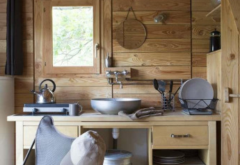 Pequeña cocina de madera con fregadero y utensilios en una tienda safari en Huttopia Wattwiller, Francia.