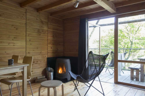 Interior acogedor de tienda safari en Huttopia Wattwiller, Francia, con estufa de leña y muebles de madera.