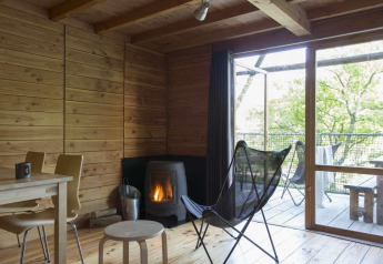 Interior acogedor de tienda safari en Huttopia Wattwiller, Francia, con estufa de leña y muebles de madera.