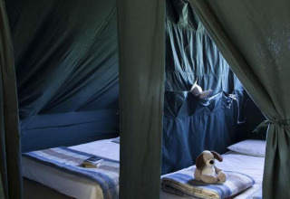 Interiør af Cahutte-safari telt på Huttopia Wattwiller med to senge, tøjdyr og børnebog på gulvet.