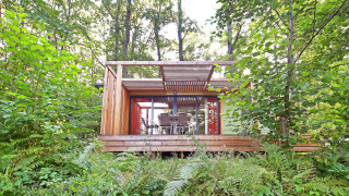 Mobile home Vancouver chalet in het bos met brede houten veranda en tuinmeubilair tussen het groen.