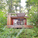 Casa móvil Vancouver en el bosque con una amplia terraza de madera y muebles de exterior rodeada de vegetación.
