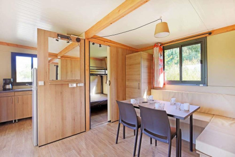 Interior luminoso y moderno de casa móvil con comedor, cocina y litera en Huttopia Wattwiller, Francia.