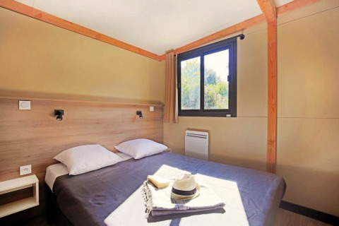 Slaapkamer in Mobile Home Vancouver met dubbel bed, twee kussens, raam, gordijn en zonlicht.