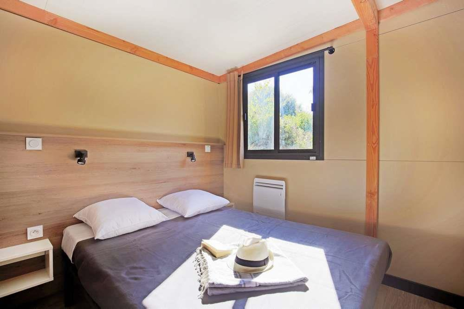 Slaapkamer in Mobile Home Vancouver met tweepersoonsbed, twee kussens, raam, gordijn en zonlicht.