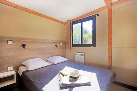 Dormitorio en Mobile home Vancouver con cama doble, dos almohadas, ventana, cortina y luz solar.