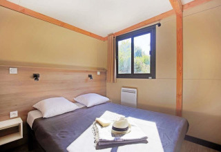 Chambre du Mobile Home Vancouver avec un lit double, deux oreillers, une fenêtre, rideau et soleil.