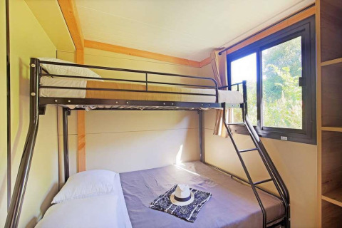 Habitación luminosa en una casa móvil con literas metálicas y ventana en Huttopia Wattwiller, Francia.