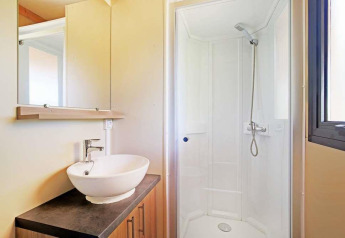 Bathroom in Mobile home Vancouver at Huttopia Wattwiller, France, featuring a shower, sink, and window.