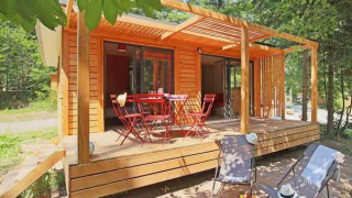 Cabaña Chalet Ottawa de madera con terraza, mesa y sillas rojas más tumbonas, rodeada de árboles.