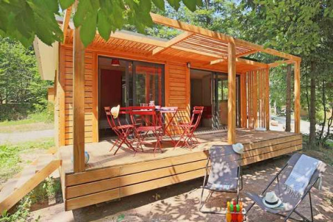 Cabaña Chalet Ottawa de madera con terraza, mesa y sillas rojas más tumbonas, rodeada de árboles.