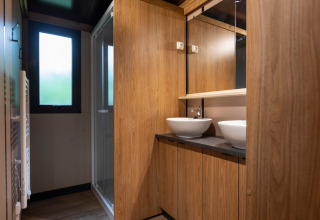 Baño moderno con dos lavabos, paneles de madera y ducha en Chalet Ottawa, Huttopia Wattwiller, Francia.