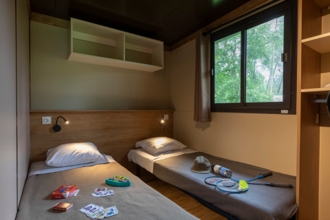 Dos camas individuales en una acogedora habitación del Chalet Ottawa, Huttopia Wattwiller, Francia, con juegos y raquetas.