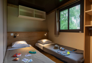 Dos camas individuales en una acogedora habitación del Chalet Ottawa, Huttopia Wattwiller, Francia, con juegos y raquetas.