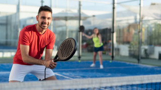 Man and woman playing padel on a sunny day at a holiday park offering glamping accommodations.