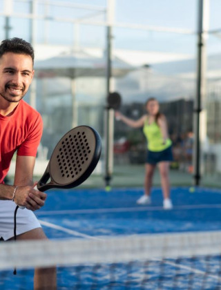 Hombre y mujer jugando pádel en un día soleado en un parque de vacaciones con alojamiento glamping.