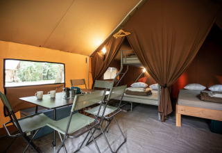 Vista interior de una tienda safari cómoda, Canadienne Tent II, con comedor y camas en Huttopia Lac de Serre Ponçon, Francia.