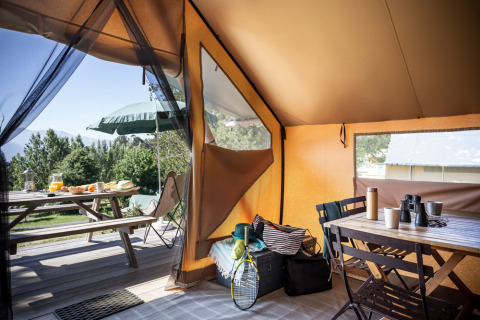 Interior de una tienda Canadienne Tent II en Huttopia Lac de Serre Ponçon con mesa de picnic y equipaje.