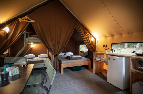 Interior de la Canadienne Tent II con camas, cocina y zona de comedor en Huttopia Lac de Serre Ponçon, Francia.