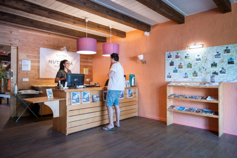 Recepción en el parque vacacional Huttopia Wattwiller en Grand Est, Francia, con huésped y recepcionista.