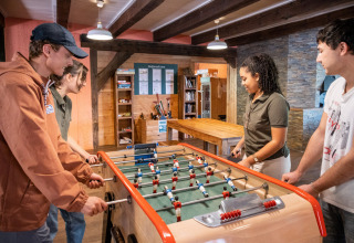 Vier jongeren spelen samen tafelvoetbal in een gezellige ruimte bij Huttopia Wattwiller, vakantiepark in Grand Est, Frankrijk.