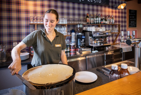 Mujer preparando crepes en una cocina del parque vacacional Huttopia Wattwiller, Grand Est, Francia.