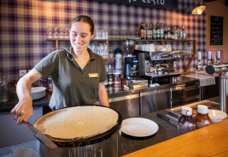 Vrouw maakt pannenkoeken in een keuken bij Huttopia Wattwiller vakantiepark, Grand Est, Frankrijk.
