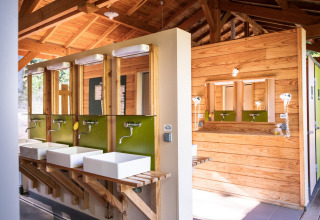 Moderne fælles badeværelsesfaciliteter med træbeklædning og håndvaske på Huttopia Wattwiller, Grand Est.